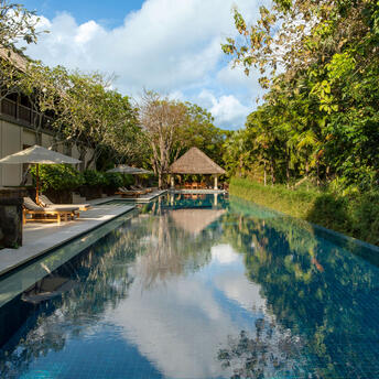 Infinity pool reflecting sky and tropical gardens at Aman Villas at Nusa Dua, Indonesia.
