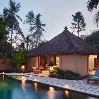 Amandari suite event space at dusk, with illuminated pavilion and reflecting pool, surrounded by tropical trees in Ubud, Bali.