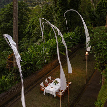 Amandari resort's Secret Garden features a suspended daybed with white cushions beneath arched wooden frames, surrounded by lush tropical greenery in Ubud, Bali.