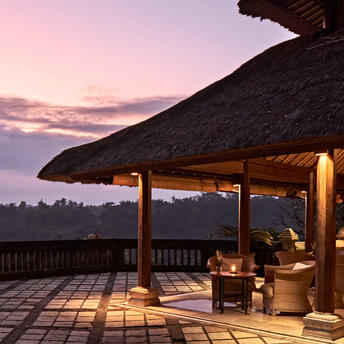 Amandari 리조트의 테라스 바에서 석양이 질 무렵 조명이 켜진 목재 구조물과 발리 계곡의 전망.