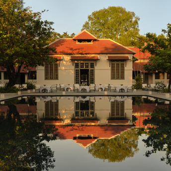 Amantaka's dining pavilion reflected in still water at dusk, set amongst mature trees.