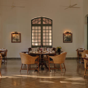 Dining room at Amantaka with round tables, wooden chairs, and large arched window framed by symmetrical artwork.