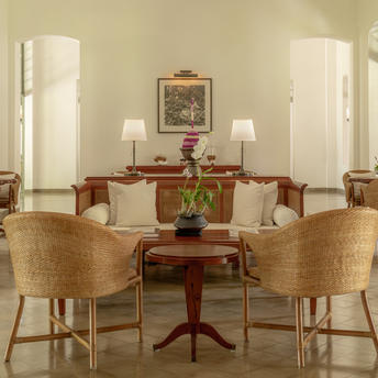 Amantaka lounge with woven chairs, wooden side table and twin table lamps beneath framed artwork.