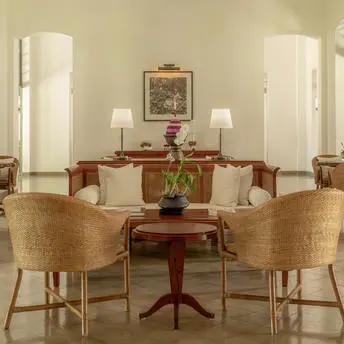Amantaka lounge with woven chairs, wooden side table and twin table lamps beneath framed artwork.