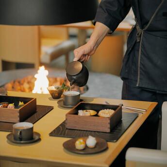 Person pouring winter afternoon tea at Aman Kyoto, with ceramic teapot and cups on wooden table.