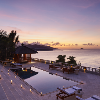 Amankila suite terrace at sunset, overlooking the Bali coastline with infinity pool and loungers.