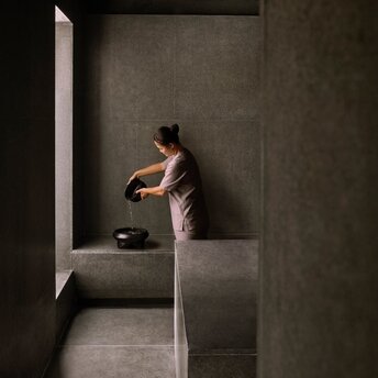 Woman in spa robe receiving hammam treatment in minimalist stone wellness room at Amanoi.