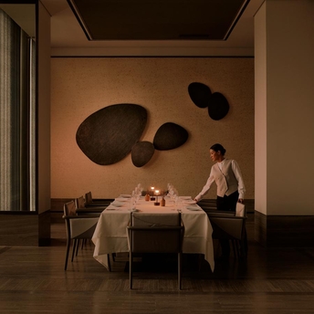 Two diners at a candlelit table beneath sculptural wall art at Aman Nai Lert Bangkok.
