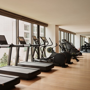 Spa and wellness gym at Aman New York featuring cardio equipment and large windows overlooking the city.