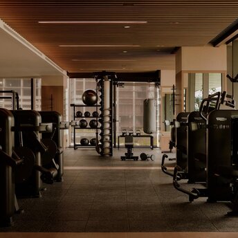 Fitness studio at Aman Nai Lert Bangkok with exercise equipment arranged along wooden-floored space beneath warm ceiling lights.