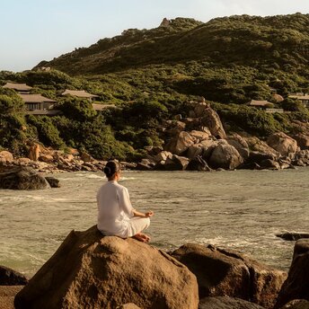 Woman meditating on rocks by the beach at Amanoi, Vietnam.