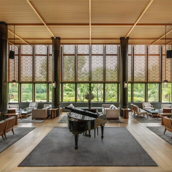 The bar at Amanyangyun, China, featuring floor-to-ceiling windows overlooking gardens, with a grand piano and comfortable seating.
