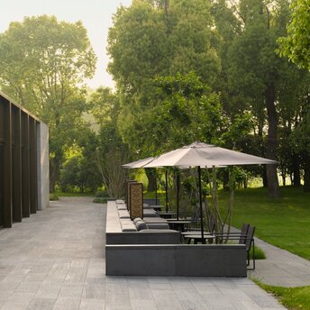 Outdoor seating area at Yinlu restaurant, Amanyangyun, with umbrellas and lounge chairs on a paved terrace surrounded by trees.