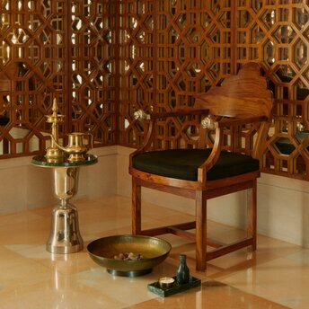 Spa treatment room at Amanbagh with wooden chair, marble floor, and golden geometric wall panels.