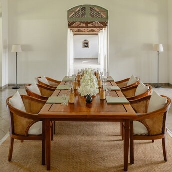 Dining room at Amantaka with oval wooden table and curved chairs, set for a meal in Luang Prabang.