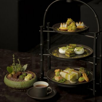 安缦东京酒店休闲厅，分层展示架摆放各式甜点和小食，绿色调装饰，配白瓷茶杯。