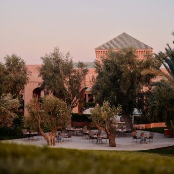 Amanjena's olive grove terrace at dawn, with traditional Moroccan architecture and palm trees.