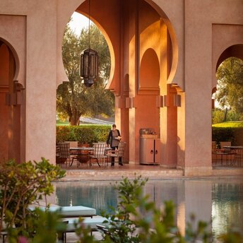 Amanjena swimming pool terrace at dusk, with arched Moroccan architecture framing the illuminated poolside.