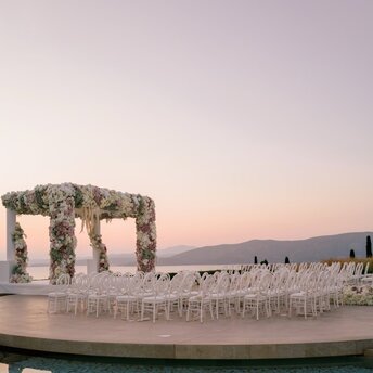 Matrimonio al tramonto presso il resort Amanzoe in Grecia, con allestimento floreale e sedie bianche.