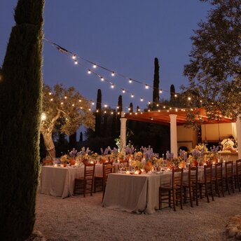 Candlelit wedding reception beneath string lights at Amanzoe resort, Greece, at dusk.