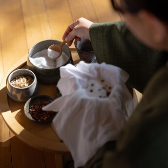 Guest prepares herbal ball at Amanemu's wellness sanctuary during seasonal spa ritual.