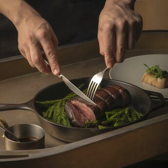 Chef plating seared meat and greens at Aman Kyoto's dining venue.