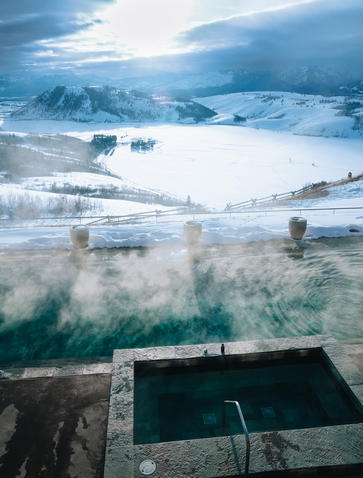 Aerial view of Amangani's plunge pool overlooking snow-covered mountains and misty valleys.