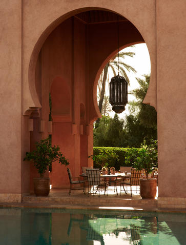 Terracotta archway framing the restaurant pool terrace at Amanjena, Morocco, with reflection in water.