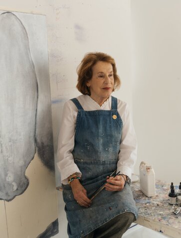 Studio portrait of Marina Karella at Amanzoe art exhibit in Greece, wearing denim apron.