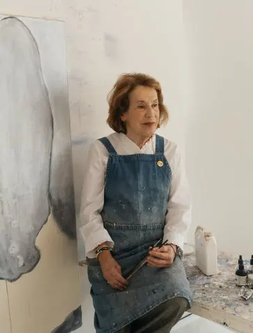 Studio portrait of Marina Karella at Amanzoe art exhibit in Greece, wearing denim apron.
