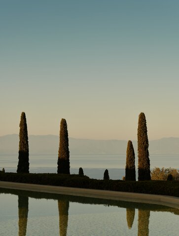 Cypress trees reflected in still water at Amanzoe, Greece, at dusk.